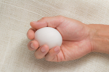 Hand holding white egg on sackcloth