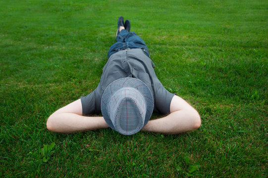 Man Lying In A Field On Green Grass With The Hat Over His Face