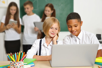 Schoolchildren sitting in classroom with laptop