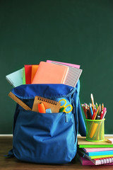School backpack with accessories on chalkboard background