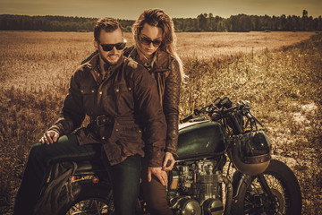 Stylish cafe racer couple on the vintage custom motorcycles in a field.