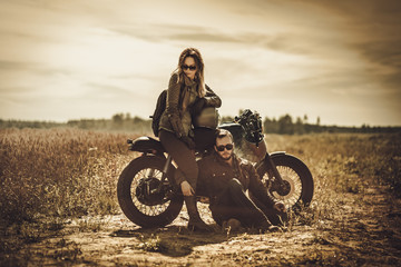 Plakat Stylish cafe racer couple on the vintage custom motorcycles in a field.