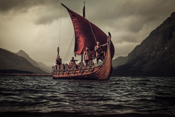 Vikings are floating on the sea on Drakkar with mountains on the - obrazy, fototapety, plakaty