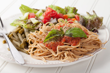 Whole wheat spaghetti topped with organic homemade marinara sauce served with green beans and an Italian side salad macro shot on white wood