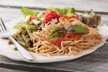Whole wheat spaghetti topped with organic homemade marinara sauce served with green beans and an Italian side salad side view