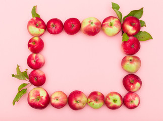 Top view on delicious red organic apples with leaves in a shape of rectangle on light pink background. Healthy food concept