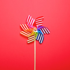 Multicolored pinwheel against red background - Minimal flat lay