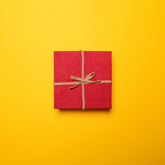 Red gift box with rope bow on yellow background - Flat lay