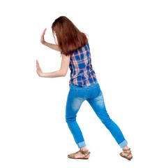 back view of woman pushes wall. backside view of person. Girl in plaid shirt shoves something in...
