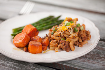 Homemade hamburger macaroni with honey glazed carrots and asparagus cooked in avocado oil taken on a weathered barn wood table
