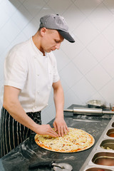Vertical photo. Male chef cook cooking a pizza on a restaurant opened kitchen