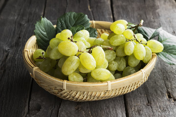 Clusters of green grapes in wattled bowl on a dark wooden backgr