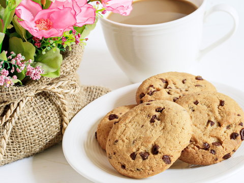 Delicious Homemade Cookies with chocolate chips, white cup of coffee and beautiful flowers on white wooden tacle