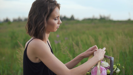 Slim girl in black dress works of flowers at sunset