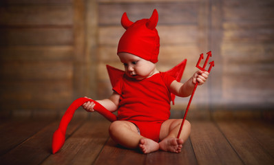 funny baby in devil halloween costume on wooden background