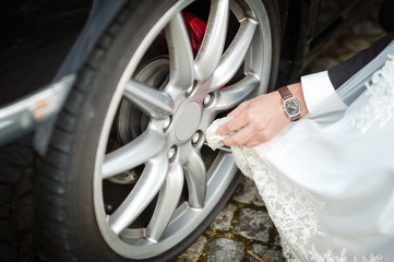 Bräutigam putzt mit Brautkleid die Felge seines Autos, Detailausschnitt