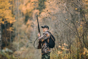 Male hunter in the woods. Man in camouflage with a backpack. Autumn forest, leaf fall.