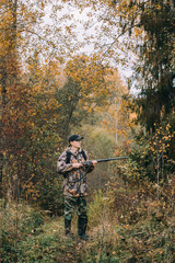 Male hunter in the woods. Man in camouflage with a backpack. Autumn forest, leaf fall.