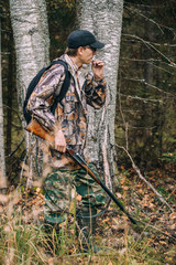 Male hunter in the woods. Man in camouflage with a backpack. Autumn forest, leaf fall.