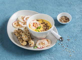 Pumpkin cream soup with apple chips and flax seed in a white bowl on a blue background. Healthy vegetarian food