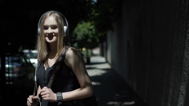 Punk girl standing on the dark pathway and listening music on headphones
