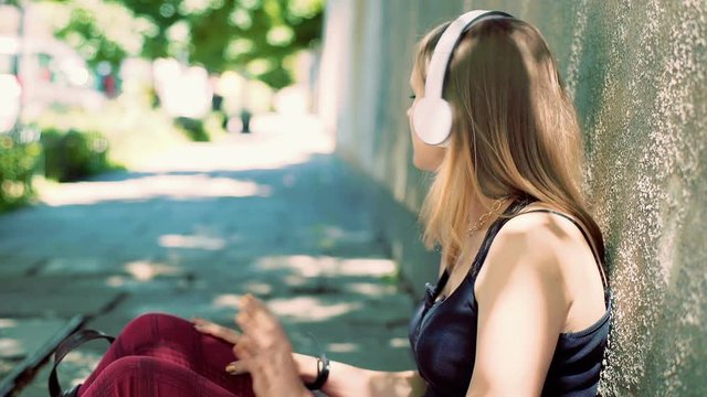 Punk girl sitting on the pathway and listening music while smiling to the camera
