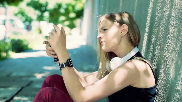 Punk girl sitting on the pathway and texting on smartphone
