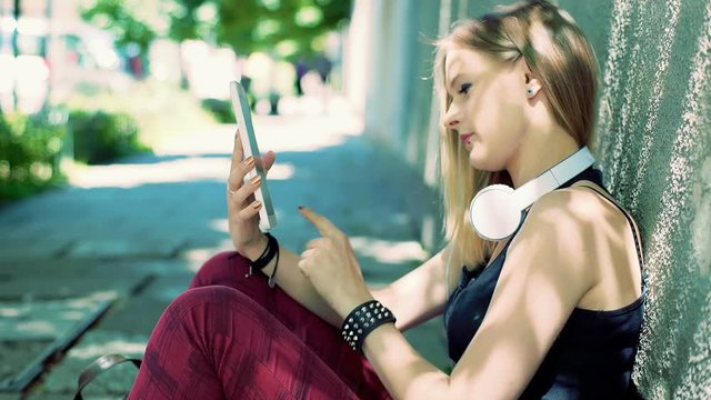Happy, punk girl sitting on the pathway and browsing internet on tablet
