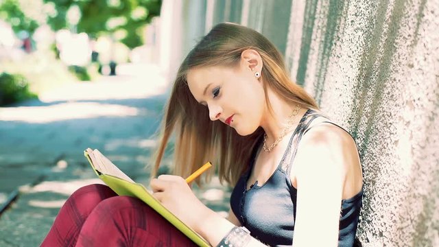 Punk girl sitting on footway and writing something in her notebook
