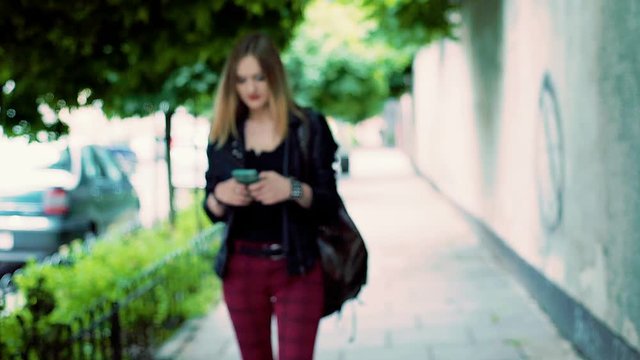 Punk girl walking on pathway and texting message on smartphone
