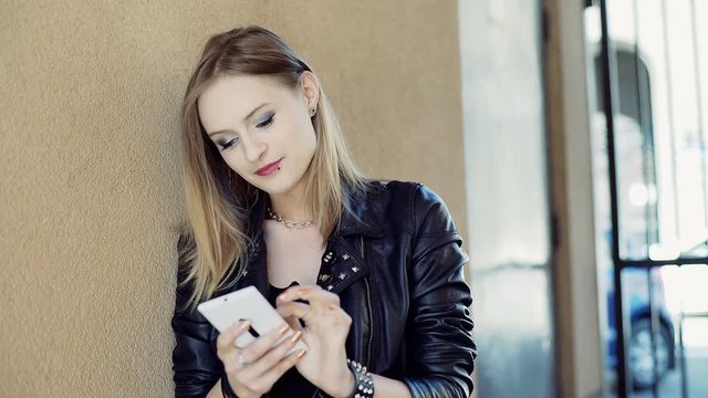 Punk girl texting on smartphone while leaning on the wall
