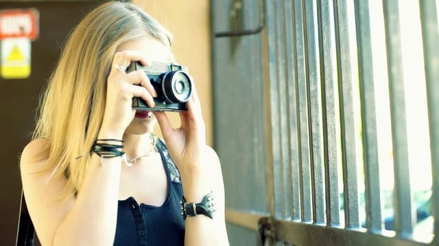Punk girl standing next to the gate and doing photos on old camera
