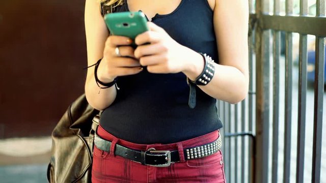 Punk girl standing outside and texting sms on smartphone

