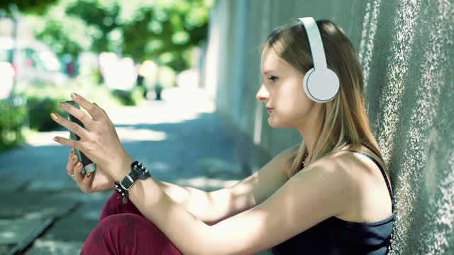 Punk girl listening music on headphones and looking on smartphone
