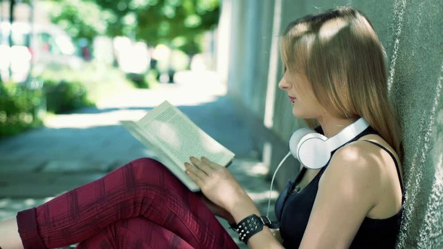 Punk girl sitting on the pathway and reading interesting book
