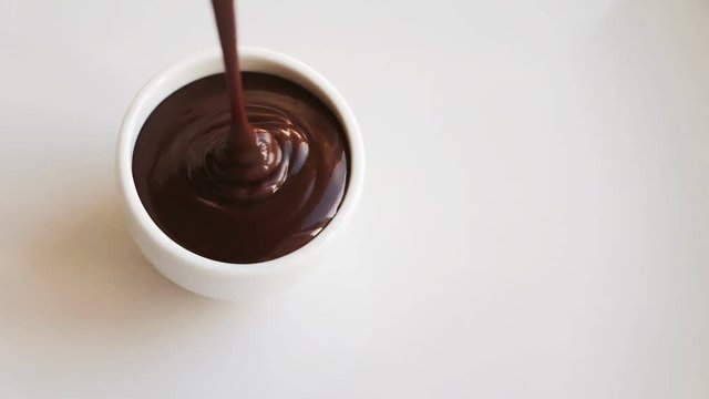 Pouring chocolate in porcelain bowl. Chocolate spilled out. White background. 