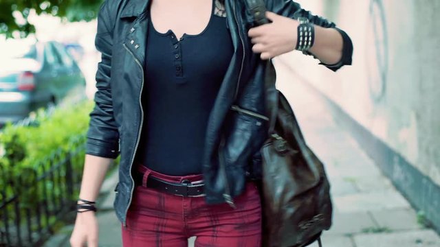Punk girl walking on pathway and looking for something in the backpack
