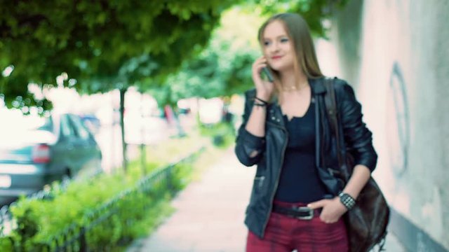 Punk girl walking on pathway and talking on cellphone, steadycam shot
