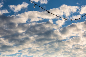 Lamp string hanging outside against a cloudy blue sky background