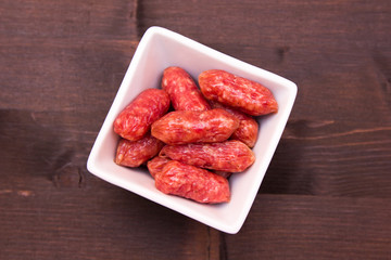 Small sausages on a square bowl on a wooden table seen from above