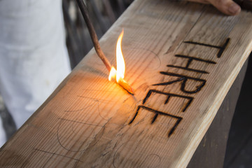 horizontal close up image of a word being burnt into the wood with a fire poker.