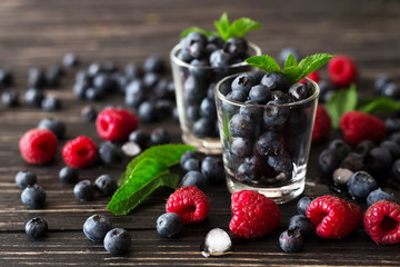 Blueberries, raspberries and mint at black wooden table.