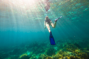 Young female snorkeling in tropical sea. Woman apnea swims in coral reef with sunbeams.
