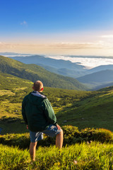 Naklejka na ściany i meble Young man standing on the top of mountain and looking at beautiful mountain landscape in sunrise time, Carpathians.