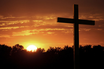 Inspirational Religious Christian Photo illustration of a Dramatic Sky with Large wooden Cross standing against very saturated colors of bright yellow sun, rich orange clouds, sunlight shafts.