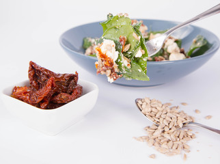 Spinach, dried tomatoes, feta cheese and sunflower seeds salad being eaten with a fork