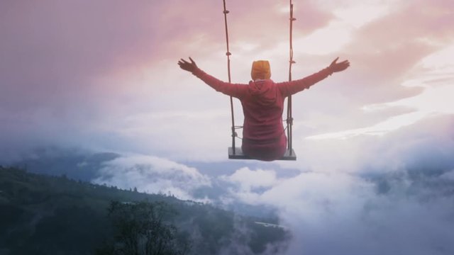 Woman on a wooden swing with open arms flying above Ecuadorian Mountains in a foggy day. Slow motion