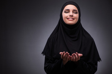 Muslim woman in black dress against dark background