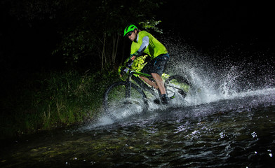 Mountain biker splashing in forest stream at night