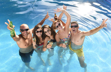 happy attractive men and women in bikini having bath at hotel resort swimming pool drinking beer